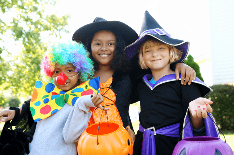 Photo of three young children in halloween costumes; a clown and two witches. Illustrating Halloween safety tips from Poison Control.